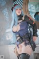 A woman with blue hair and a gun posing for a picture.