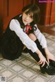 A woman in a school uniform sitting on the floor.