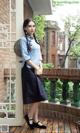 A woman in a blue shirt and black skirt standing on a balcony.