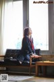 A woman sitting on a couch in front of a window.