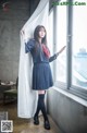 A woman in a school uniform standing by a window.