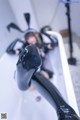 A woman in a black latex outfit is sitting in a bathtub.