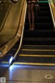 A woman in a black dress is walking down an escalator.