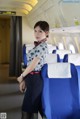 A woman in a blue and white uniform standing in an airplane.