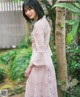 A woman in a pink dress standing next to a tree.