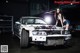 A woman standing next to a wrecked car in a garage.