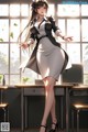 A woman in a white dress and black jacket standing in front of a window.