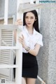 A woman in a white shirt and black skirt leaning against a wall.